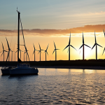 **Image:** A sprawling wind farm along the Polish Baltic coast at sunset, with the silhouette of Gdańsk in the distance. Sailboats should be in the foreground, highlighting the integration of traditional maritime activities with modern green energy.